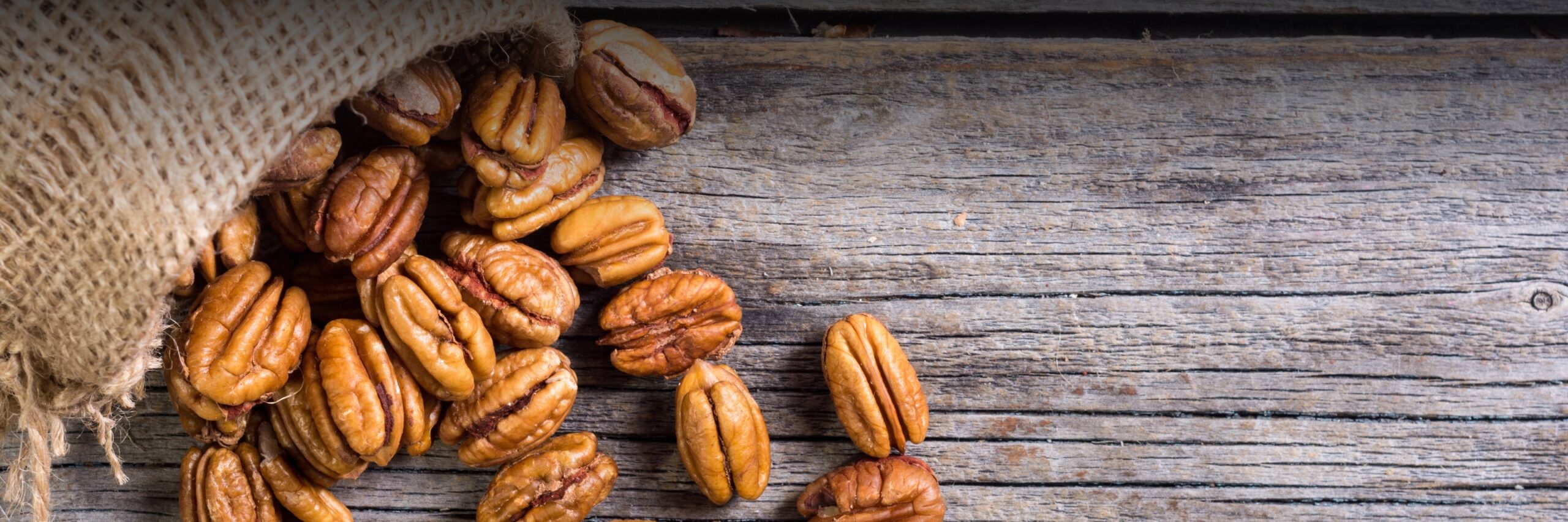 Close Up of Pecans Falling Out of Bag Against Wood Background